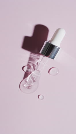 Vertical-video-of-make-up-pipette-and-drops-of-serum-with-copy-space-on-pink-background