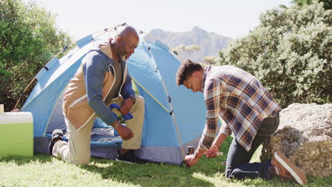 Happy-african-american-father-and-son-pitching-tent-together-in-sunny-countryside,-slow-motion
