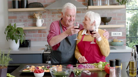 Happy-senior-caucasian-couple-cooking-dinner-drinking-red-wine-in-kitchen-at-home,-slow-motion