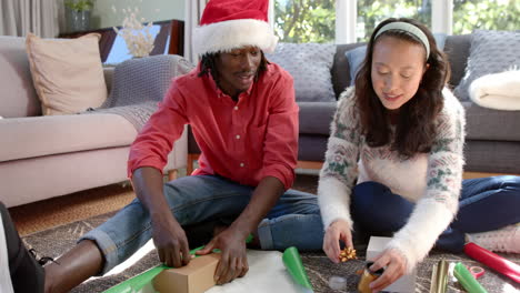 Happy-diverse-couple-sitting-on-floor-at-home-wrapping-christmas-gifts,-slow-motion