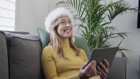 Feliz-Mujer-Birracial-Con-Sombrero-De-Santa-Usando-Tableta-Para-Videollamada-Navideña,-En-Cámara-Lenta