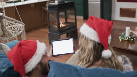 Vielfältiges-Paar-Mit-Weihnachtsmannmützen,-Das-Ein-Tablet-Mit-Platz-Zum-Kopieren-Auf-Dem-Bildschirm-Verwendet,-In-Zeitlupe