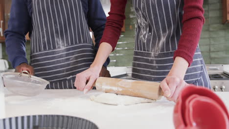 Happy-diverse-couple-standing-in-kitchen,-sifting-flour-and-rolling-dough,slow-motion