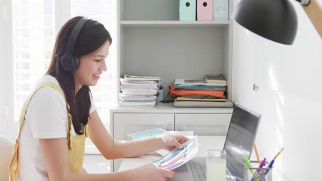 Glückliche-Biracial-Frau-Mit-Kopfhörern,-Die-Am-Schreibtisch-Einen-Videoanruf-über-Den-Laptop-Führt-Und-Zu-Hause-Arbeitet,-Zeitlupe