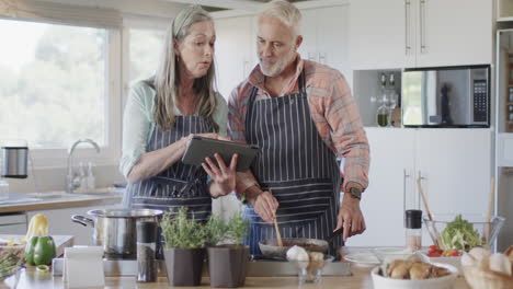 Middle-aged-caucasian-couple-with-tablet,-preparing-meal,-cooking-in-kitchen-at-home,-slow-motion