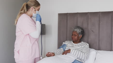 Caucasian-female-nurse-in-mask-checking-pressure-of-senior-african-american-woman,-slow-motion