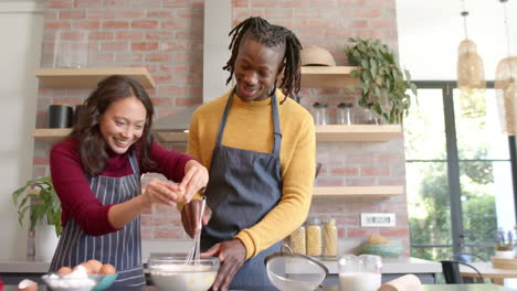 Happy-diverse-couple-in-aprons-baking-in-sunny-kitchen,-copy-space,-slow-motion