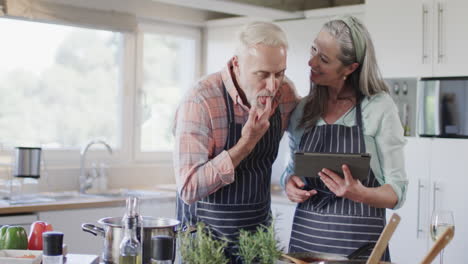 Middle-aged-caucasian-couple-using-tablet,-preparing-meal,-cooking-in-kitchen-at-home,-slow-motion