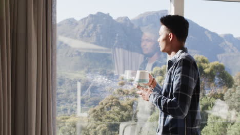 Afroamerikanischer-Mann-Trinkt-Kaffee-Am-Fenster-Mit-Sonnigem-Blick-Auf-Die-Berge,-Kopierraum,-Zeitlupe