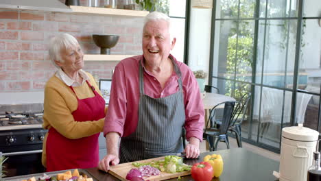 Happy-senior-caucasian-couple-wearing-aprons-cooking-dinner-in-kitchen-at-home,-slow-motion