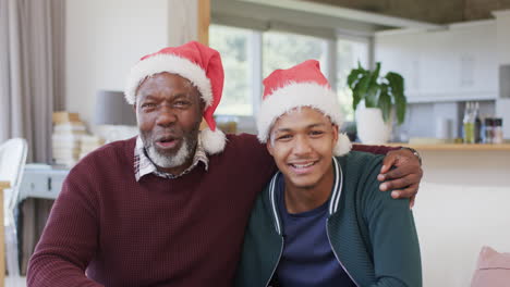 Feliz-Padre-E-Hijo-Afroamericanos-Con-Sombreros-Navideños-Teniendo-Videollamadas-Y-Abrazándose,-Cámara-Lenta