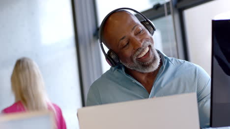 African-american-businessman-using-headphones-and-talking-in-office-with-copy-space