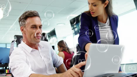 Animation-of-6g-texts-in-bubbles-over-diverse-coworkers-discussing-reports-on-laptop-in-office