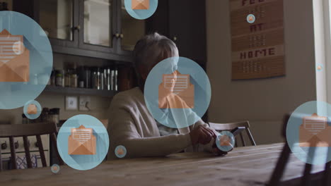 Animation-Von-Briefumschlagsymbolen-In-Kreisen-über-Einer-älteren-Frau-Mit-Gemischter-Abstammung,-Die-Zu-Hause-Auf-Ihrem-Smartphone-Scrollt