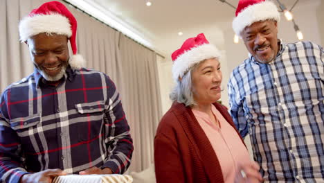 Happy-diverse-senior-friends-in-santa-outfit-and-christmas-hats-exchanging-gifts,-slow-motion