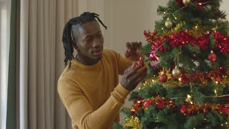 Feliz-Hombre-Afroamericano-Con-Rastas-Decorando-El-árbol-De-Navidad,-Cámara-Lenta