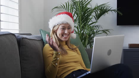 Happy-biracial-woman-wearing-santa-hat-using-laptop-for-christmas-video-call,-in-slow-motion