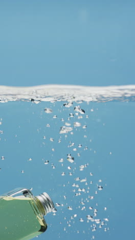 Vertikales-Video-Einer-Kosmetikflasche,-Die-Ins-Wasser-Fällt,-Mit-Kopierraum-Auf-Blauem-Hintergrund