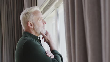 Portrait-of-middle-aged-thoughtful-caucasian-man-by-window-at-home-with-copy-space