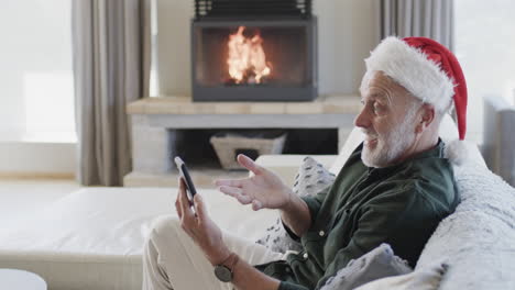 Middle-aged-caucasian-man-in-santa-hat-using-smartphone-at-christmas-at-home,-slow-motion