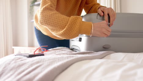 Caucasian-woman-packing-and-zipping-suitcase-on-bed-at-home,-copy-space,-slow-motion