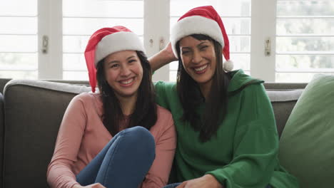 Portrait-of-happy-biracial-mother-and-adult-daughter-in-christmas-hats,-copy-space,-slow-motion