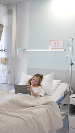 Vertical-video-of-caucasian-girl-patient-in-hospital-bed-using-tablet,-copy-space,-slow-motion