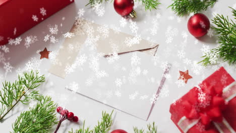Animation-of-snow-falling-over-christmas-decorations-and-envelopes