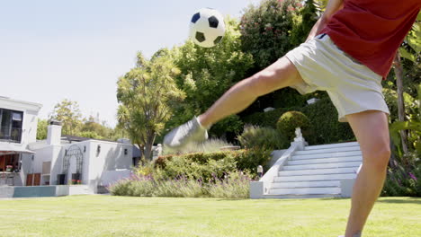 Focused-biracial-man-practicing-football-skills-in-sunny-garden,-copy-space,-slow-motion