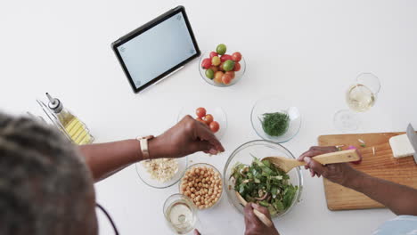 Senior-african-american-female-friends-making-salad,-using-tablet-with-copy-space,-slow-motion