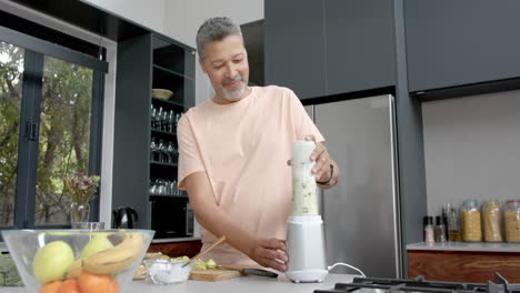 Happy-senior-biracial-man-blending-healthy-smoothie-in-kitchen,-copy-space,-slow-motion