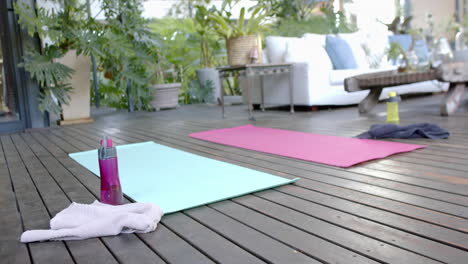 Water-bottle,-towel-and-exercise-mats-on-sunny-terrace