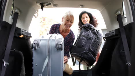 Two-happy-diverse-senior-women-putting-suitcase-and-backpack-into-car-on-sunny-day,-slow-motion