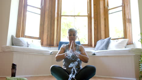 Incense-sticks-with-smoke-trails-over-focused-senior-biracial-woman-meditating-at-home
