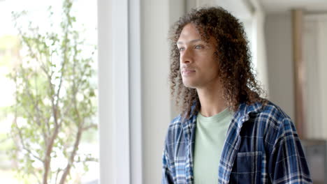 Thoughtful-biracial-man-with-long-curly-hair-in-sunny-living-room-at-home,-copy-space,-slow-motion