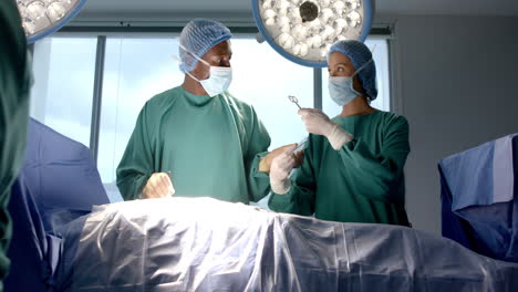 Diverse-female-and-male-surgeons-in-masks-passing-surgical-tools-during-operation,-slow-motion