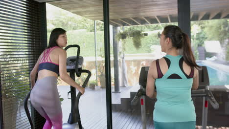 Happy-asian-female-friends-exercising-and-discussing-in-sunny-home-gym,-slow-motion