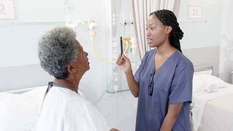 African-american-female-doctor-testing-eyes-of-senior-female-patient-in-hospital-room,-slow-motion