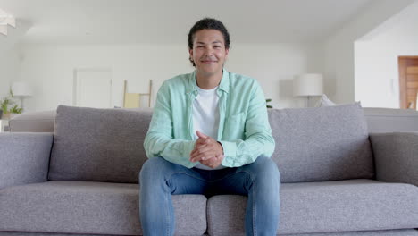 Portrait-of-happy-biracial-man-sitting-on-sofa-smiling-in-living-room,-copy-space,-slow-motion