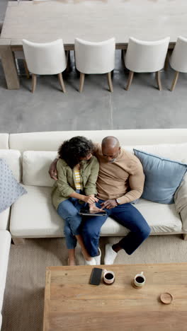 Vertical-video-of-happy-diverse-mature-couple-on-couch-using-tablet,-copy-space,-slow-motion