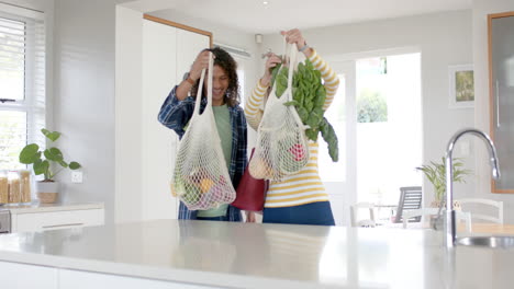 Happy-diverse-couple-carrying-and-unpacking-grocery-shopping-bags-in-kitchen,-slow-motion