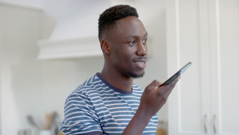 Glücklicher-Afroamerikanischer-Mann-Mit-Smartphone-Und-Lächeln-In-Sonniger-Küche,-Zeitlupe