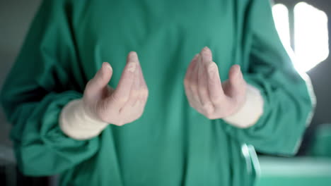 Midsection-of-caucasian-male-surgeon-wearing-medical-gloves-in-operating-theatre,-slow-motion
