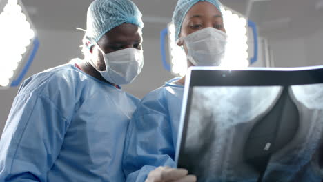 African-american-male-and-female-surgeons-looking-at-x-ray-scans-in-operating-theatre,-slow-motion