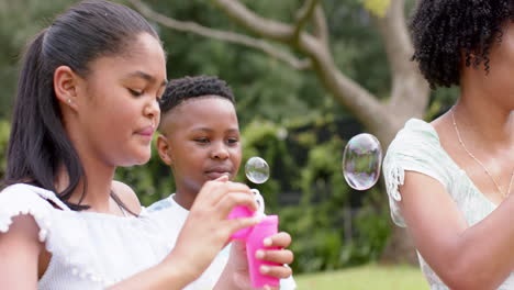 Happy-african-american-mother,-daughter-and-son-blowing-bubbles-in-garden,-slow-motion