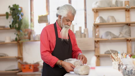 Happy-biracial-potter-with-long-beard-working-and-smiling-in-pottery-studio,-slow-motion
