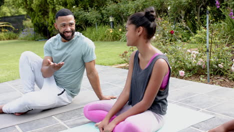 Happy-african-american-father-daughter-and-son-doing-yoga-sitting-in-garden-talking,-slow-motion