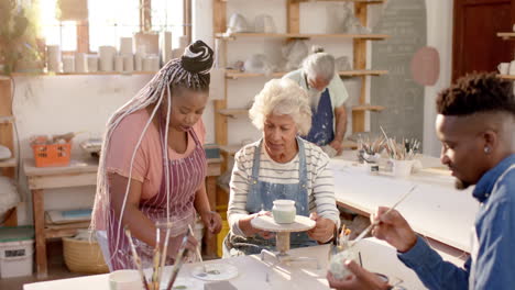 Happy-diverse-group-of-potters-glazing-clay-jugs-and-discussing-in-pottery-studio