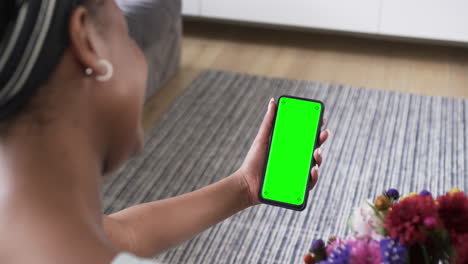 African-american-woman-holding-smartphone-with-copy-space-on-green-screen