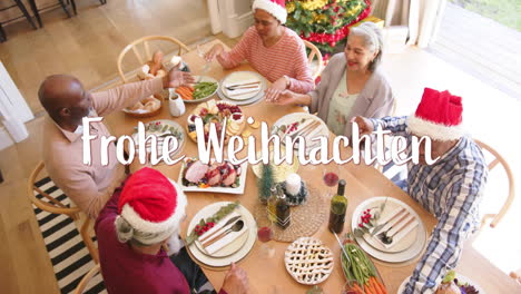 Animation-Of-Frohe-Weihnachten-Text-Over-Diverse-Senior-Friends-Sitting-At-Table-At-Christmas